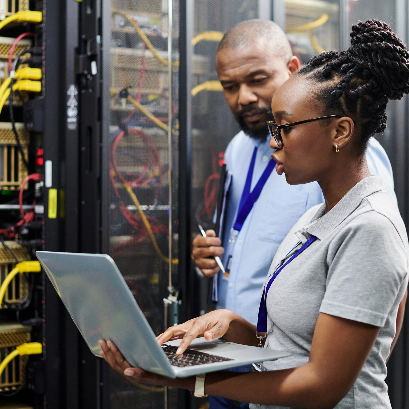 Shot of two technicians working together on a laptop in a server room.