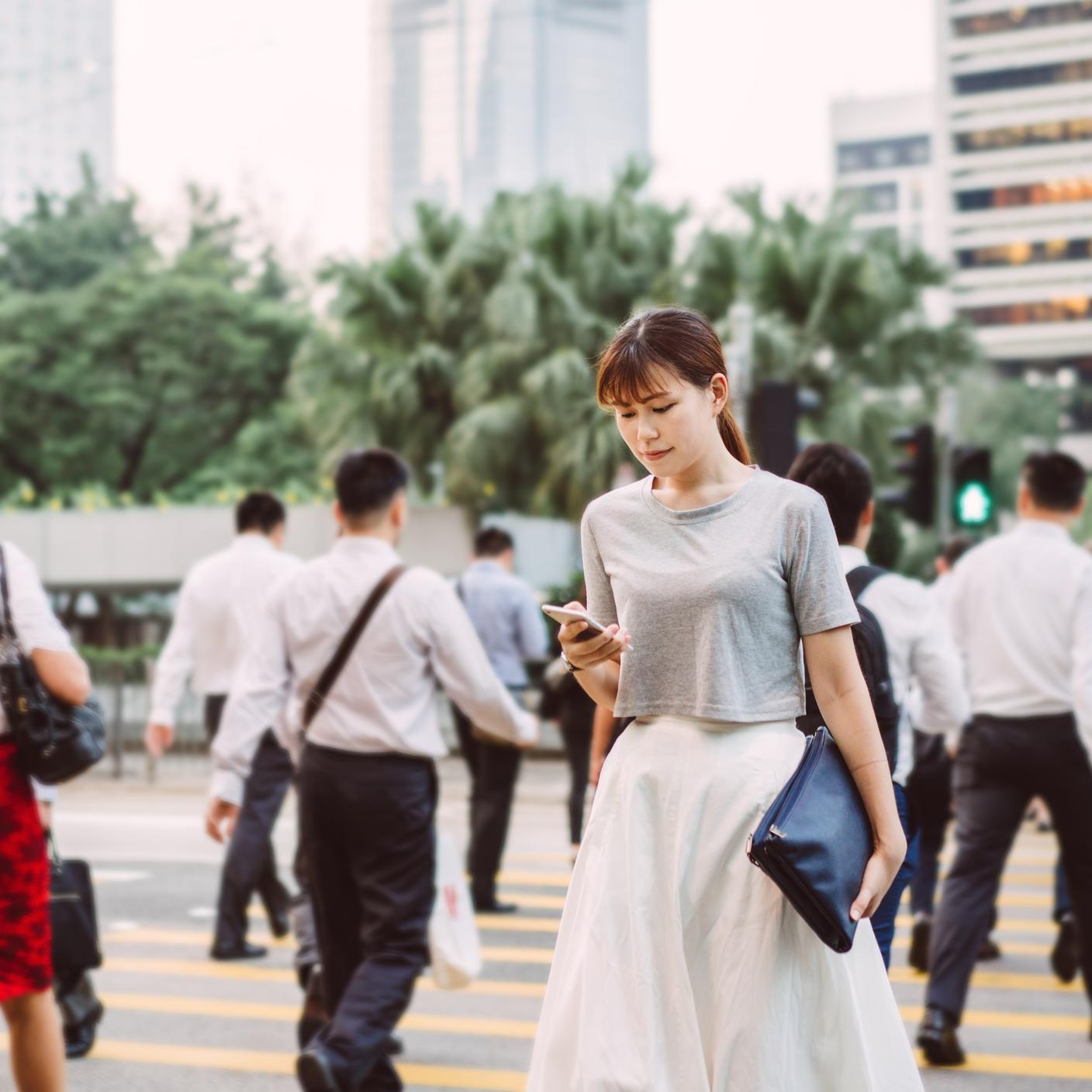 Une femme utilise son téléphone intelligent en traversant la route dans le quartier central des affaires