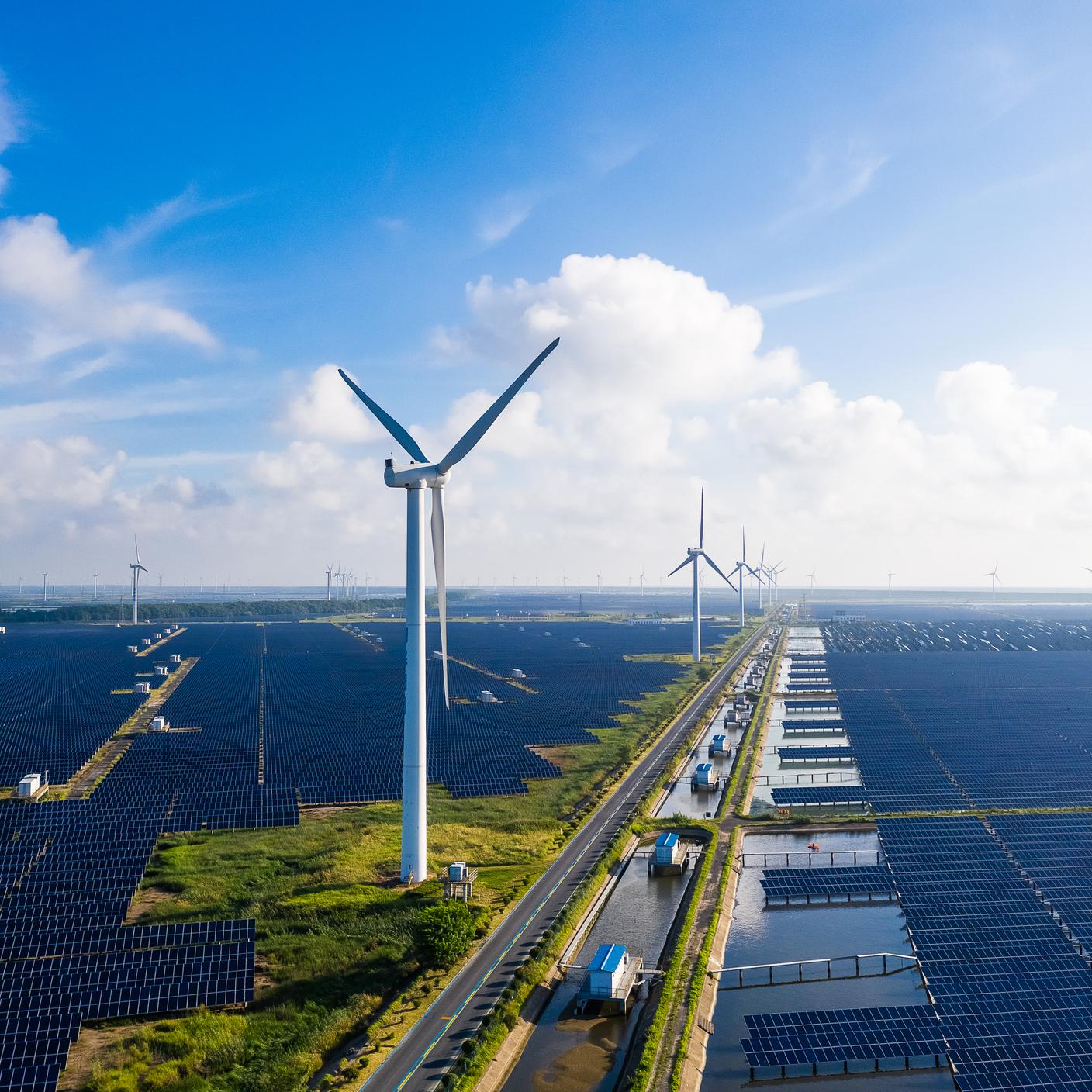 Düzlüklerde güneş enerjisi santralleri, uzakta rüzgâr türbinleri. Çin'in Jiangsu Bölgesinde bulunan Yancheng Şehri.