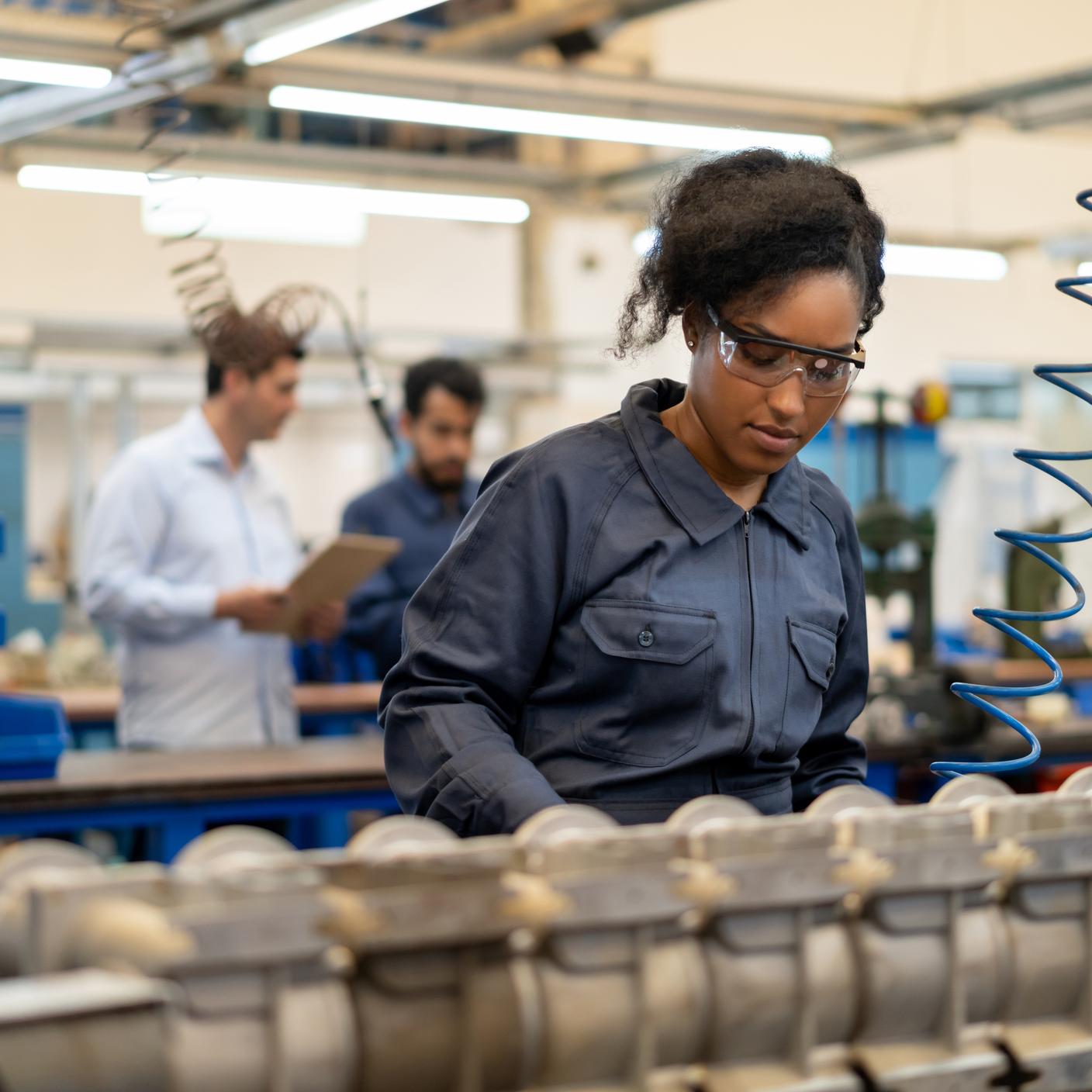 Junge afroamerikanische Frau arbeitet bei der Montage von Wasserpumpen in einer Fabrik - zufällige Personen im Hintergrund