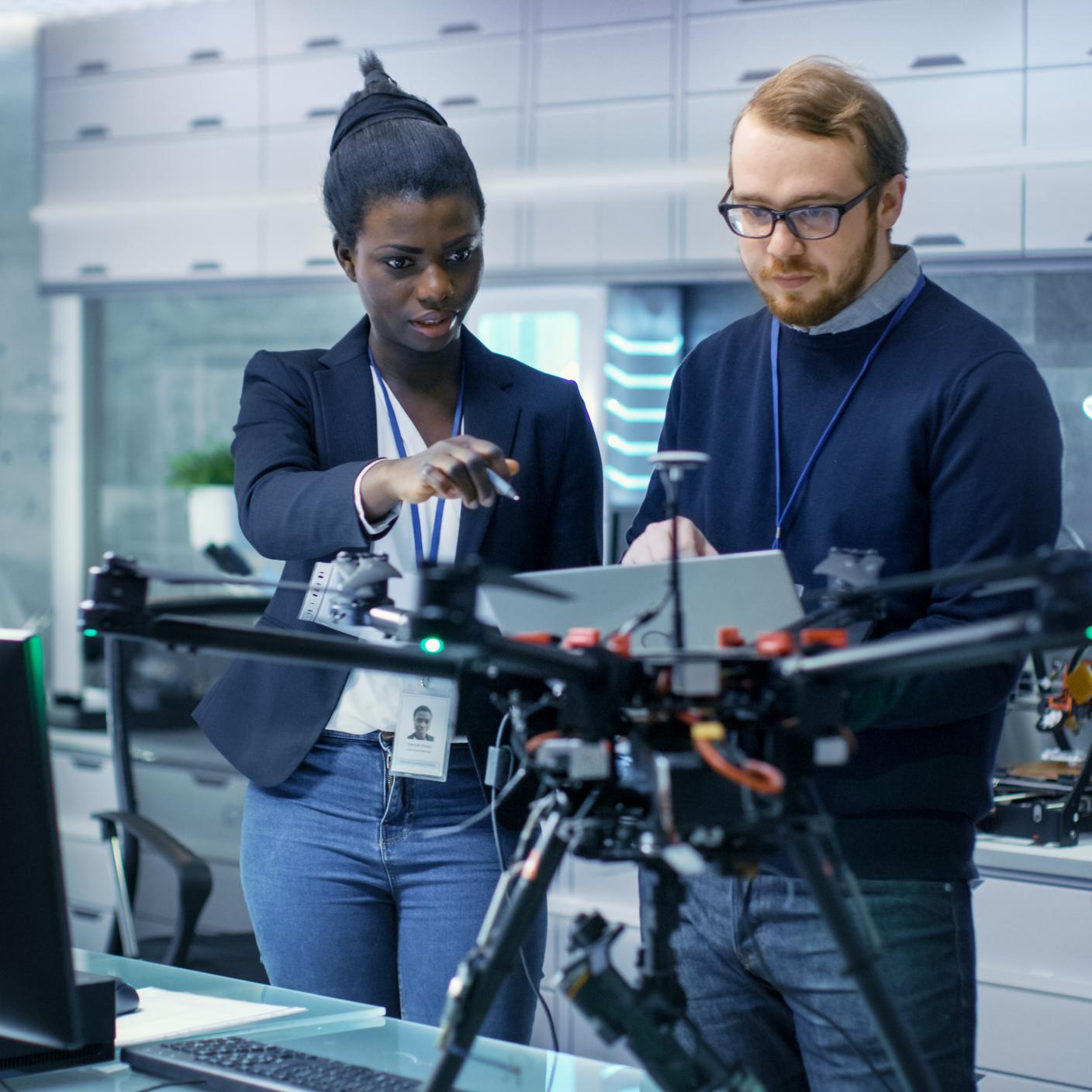 Two engineers working on a drone project with help of laptop and taking notes.