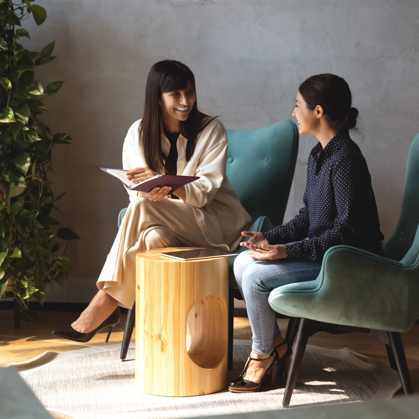 Dos colegas simpáticas sentadas en sillones disfrutan de una agradable conversación y comparten información en una reunión informal en el vestíbulo moderno de la oficina. Mujeres de negocios indias y caucásicas conversan durante el flujo de trabajo (recortado)