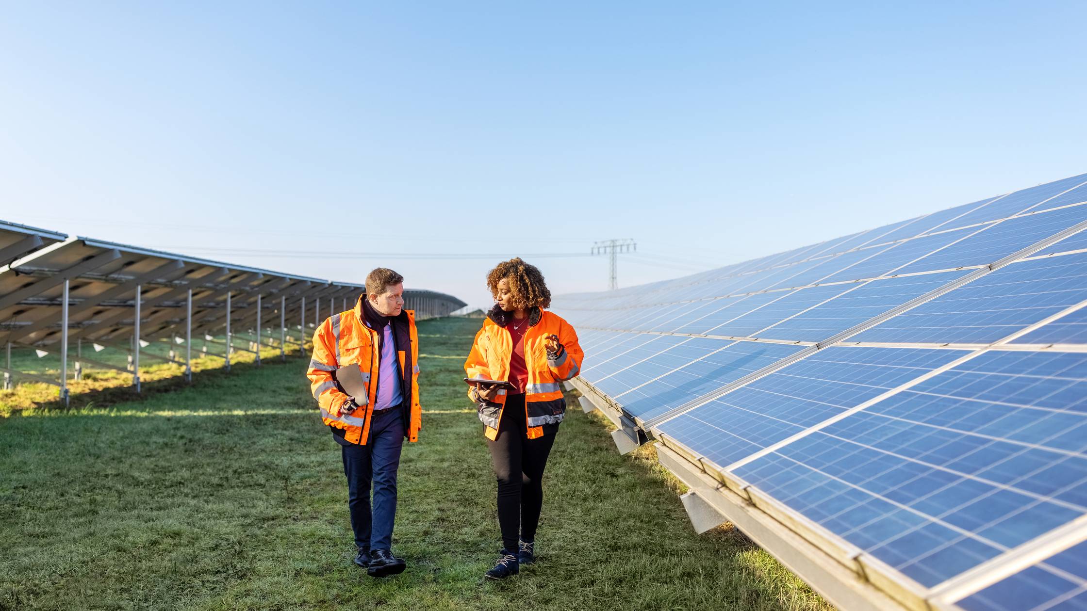 Dos técnicos con ropa reflectante caminan entre filas de paneles fotovoltaicos en un parque solar.