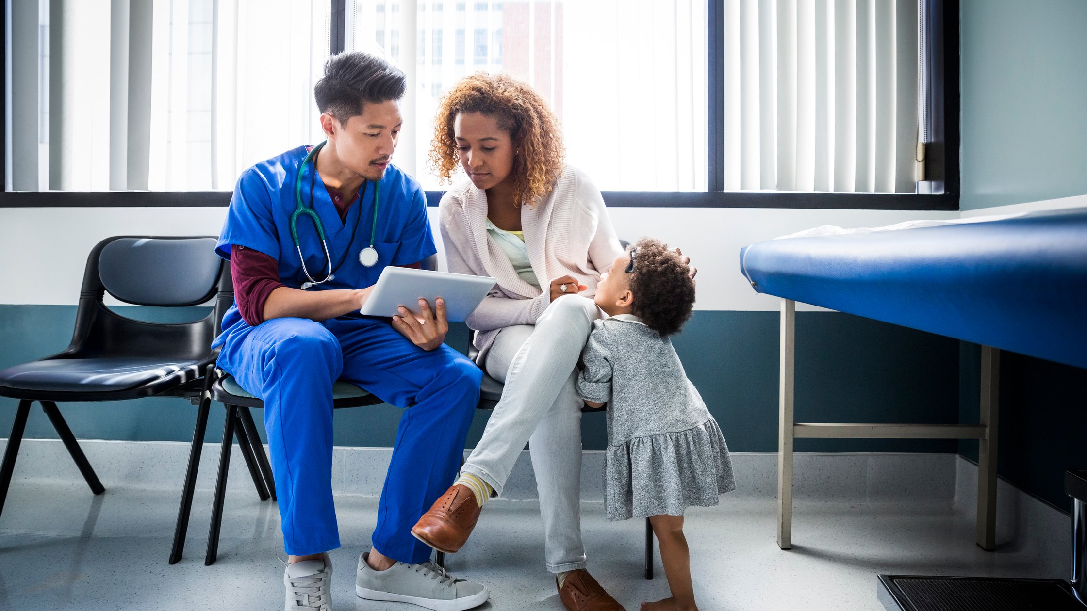 Male nurse showing digital tablet to mother by toddler in hospital